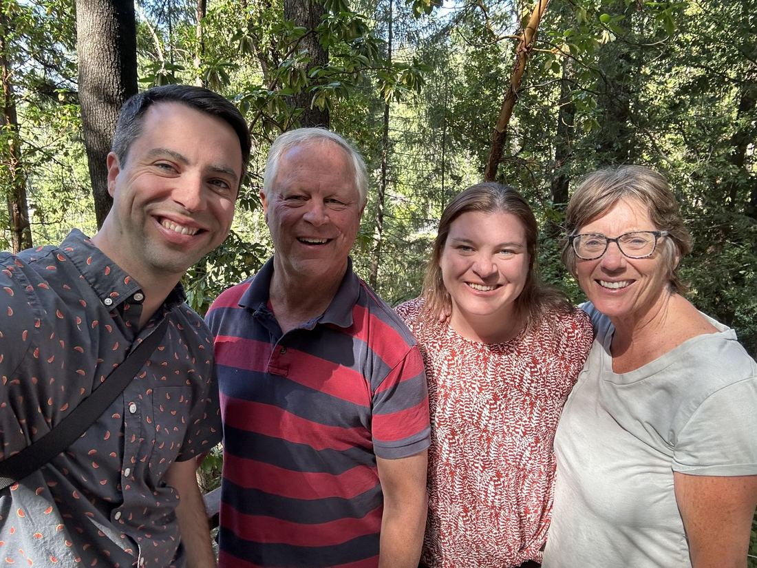 Terry and Liz with family, smiling together among the trees