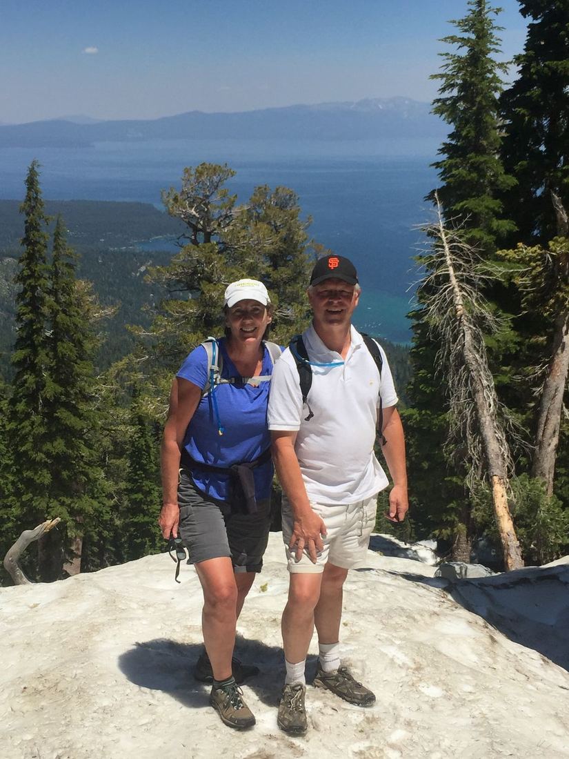 Terry and Liz on a mountain hike with a lake and forest far below