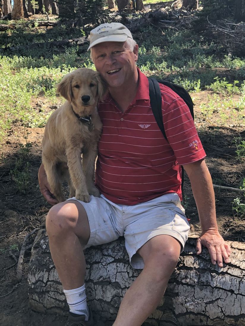 Terry sitting on a log along a trail with a golden retriever puppy